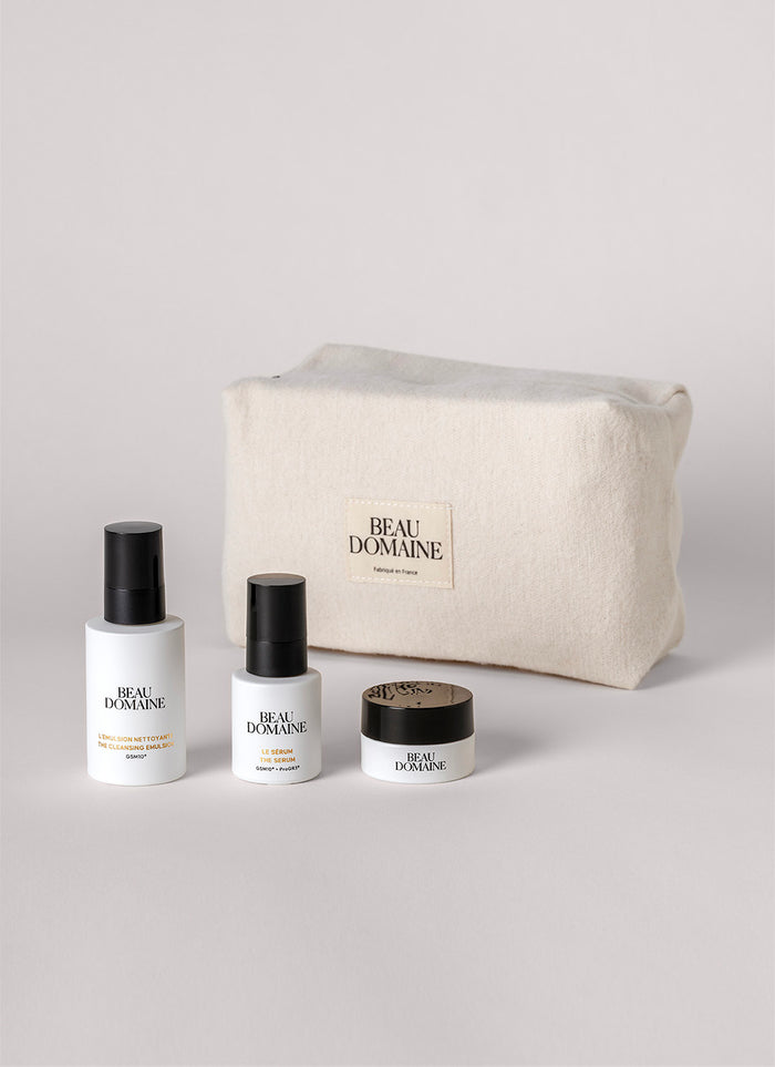 Cosmetic set with bottles and a jar in front of a 'Beau Domaine' pouch on a light gray background